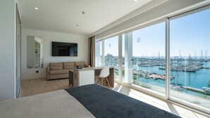 Ein modernes Schlafzimmer mit einem großen Bett, einem Schreibtisch, einer Couch und Blick auf eine Marina.