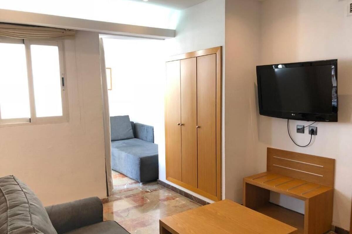 Een kamer met een bank, een houten tafel, een aan de muur bevestigde televisie en een kledingkast.