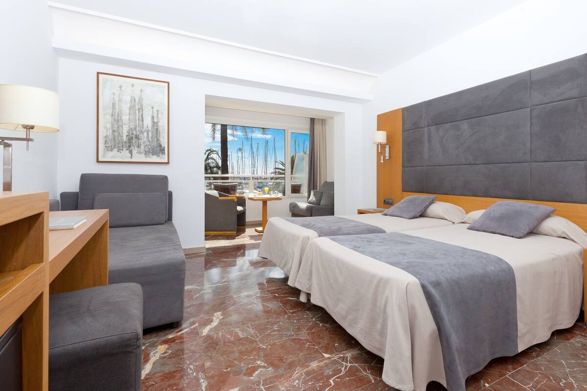 Een hotelkamer met twee bedden, een bank, een bureau en uitzicht op zee.