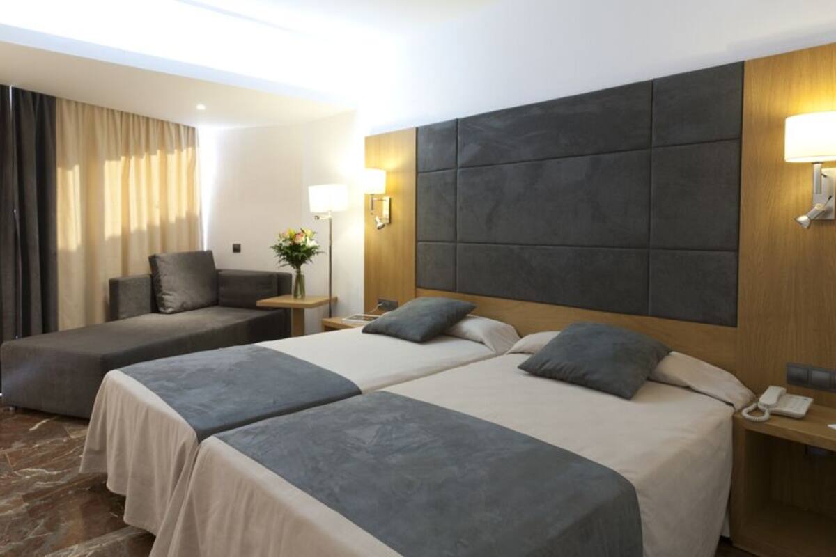Een hotelkamer met twee bedden, een bank, een nachtkastje met een telefoon en een lamp.