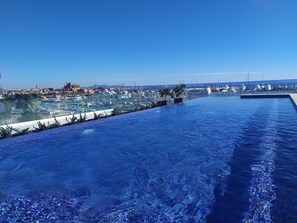 Une piscine à débordement offrant une vue sur un port de plaisance et sur le paysage urbain.