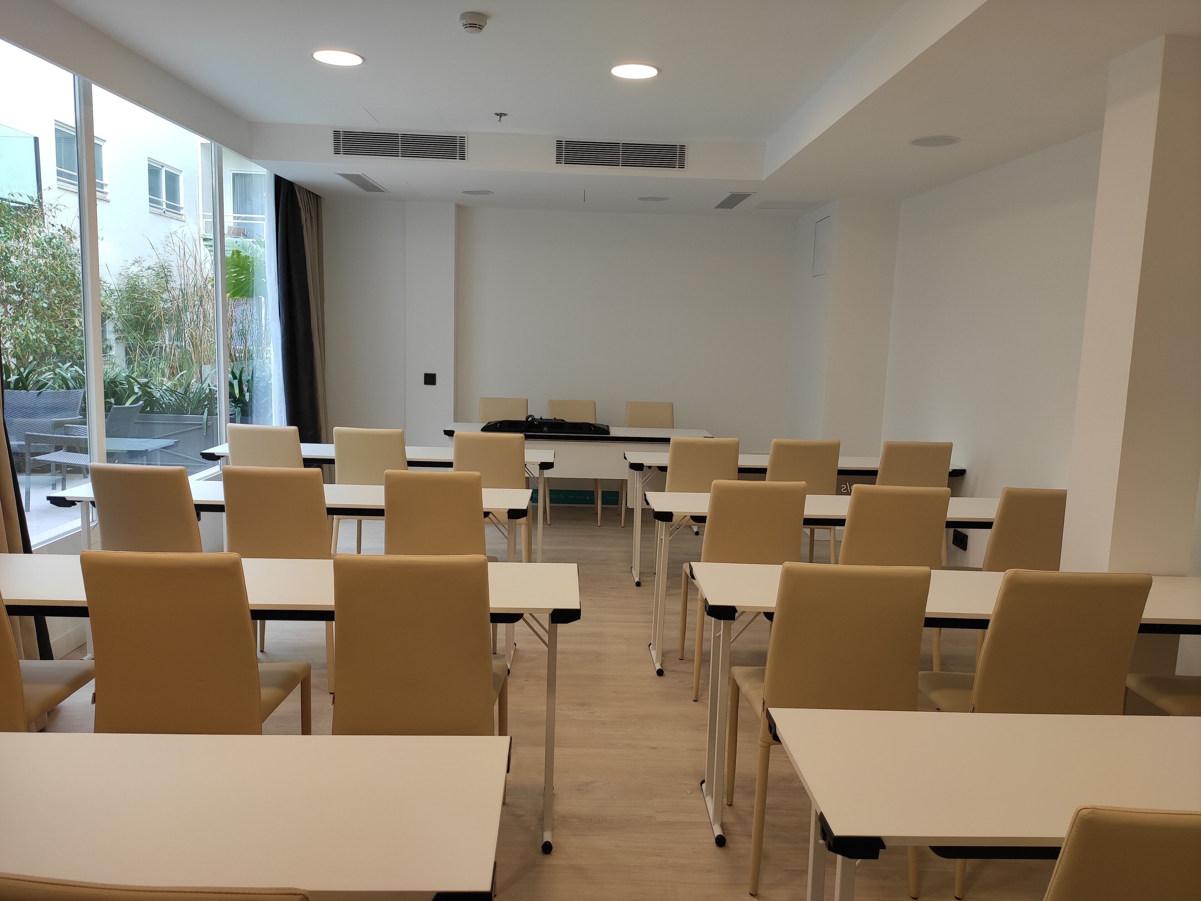 Un aula con filas de escritorios y sillas, ventanas amplias y una pizarra.