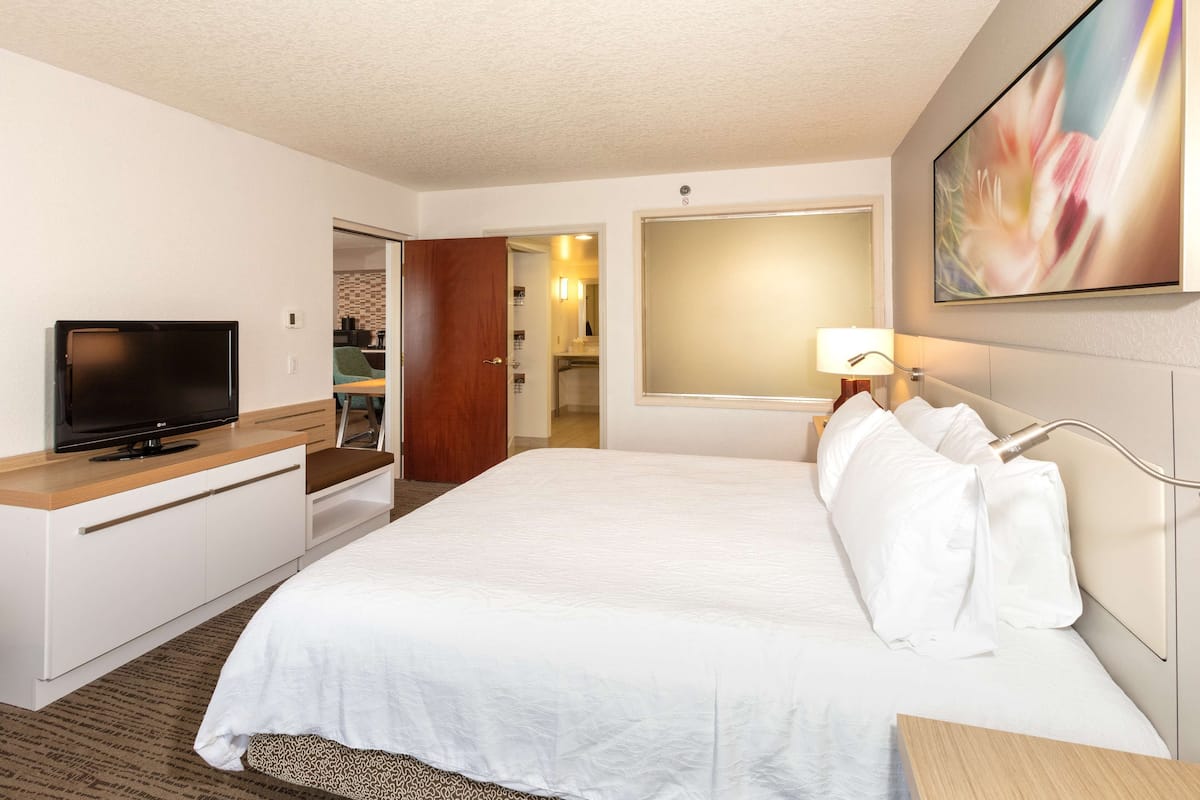A hotel room with a bed, a TV, a desk, and a bathroom visible through an open door.