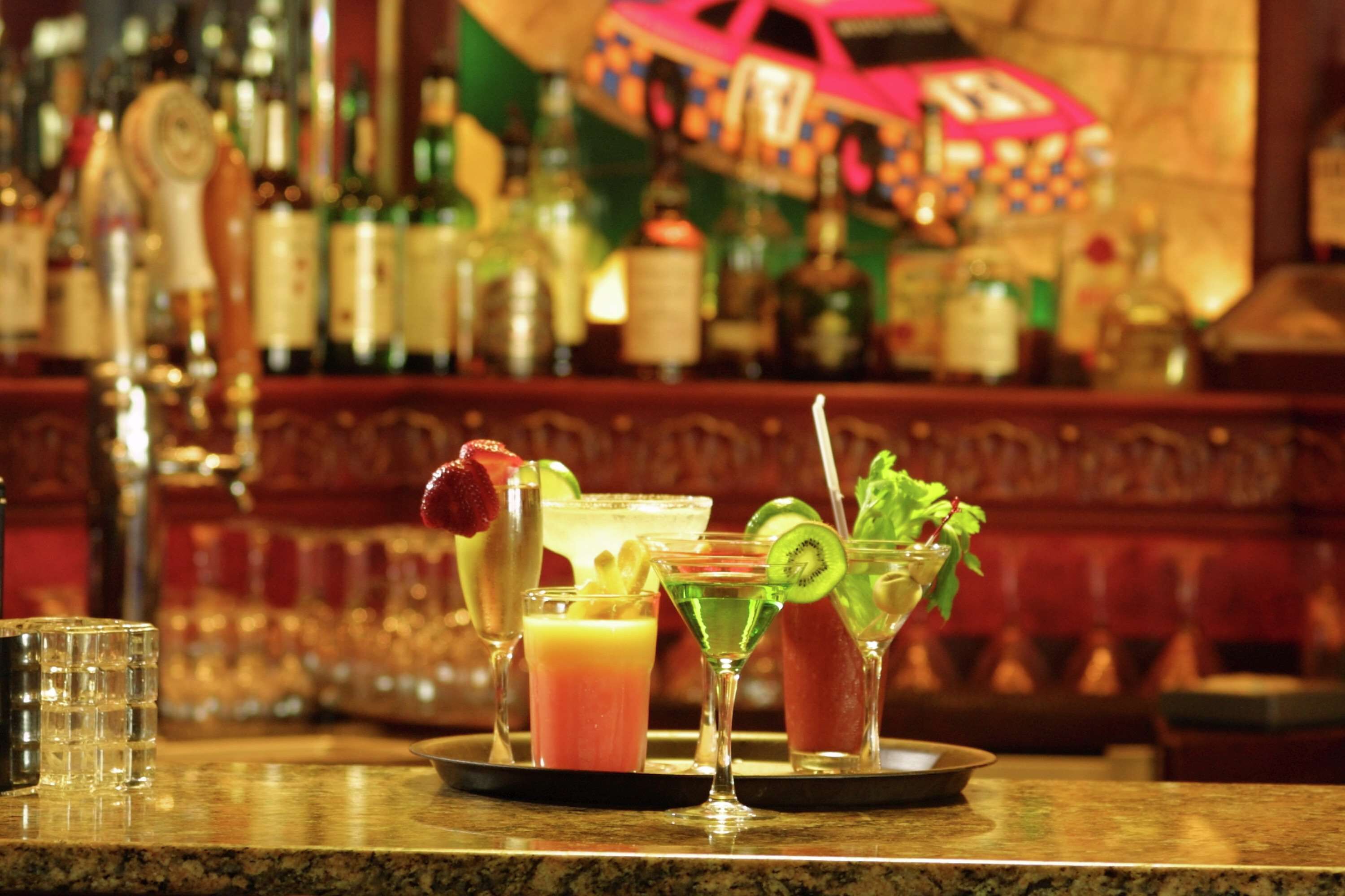 A bar counter with various cocktails and a selection of liquor bottles in the background.