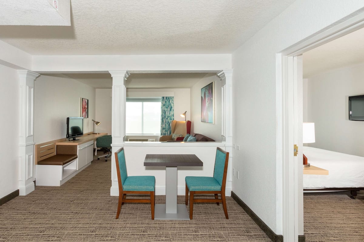 A hotel room with a desk, two chairs, a TV, a bed, and a window with curtains.