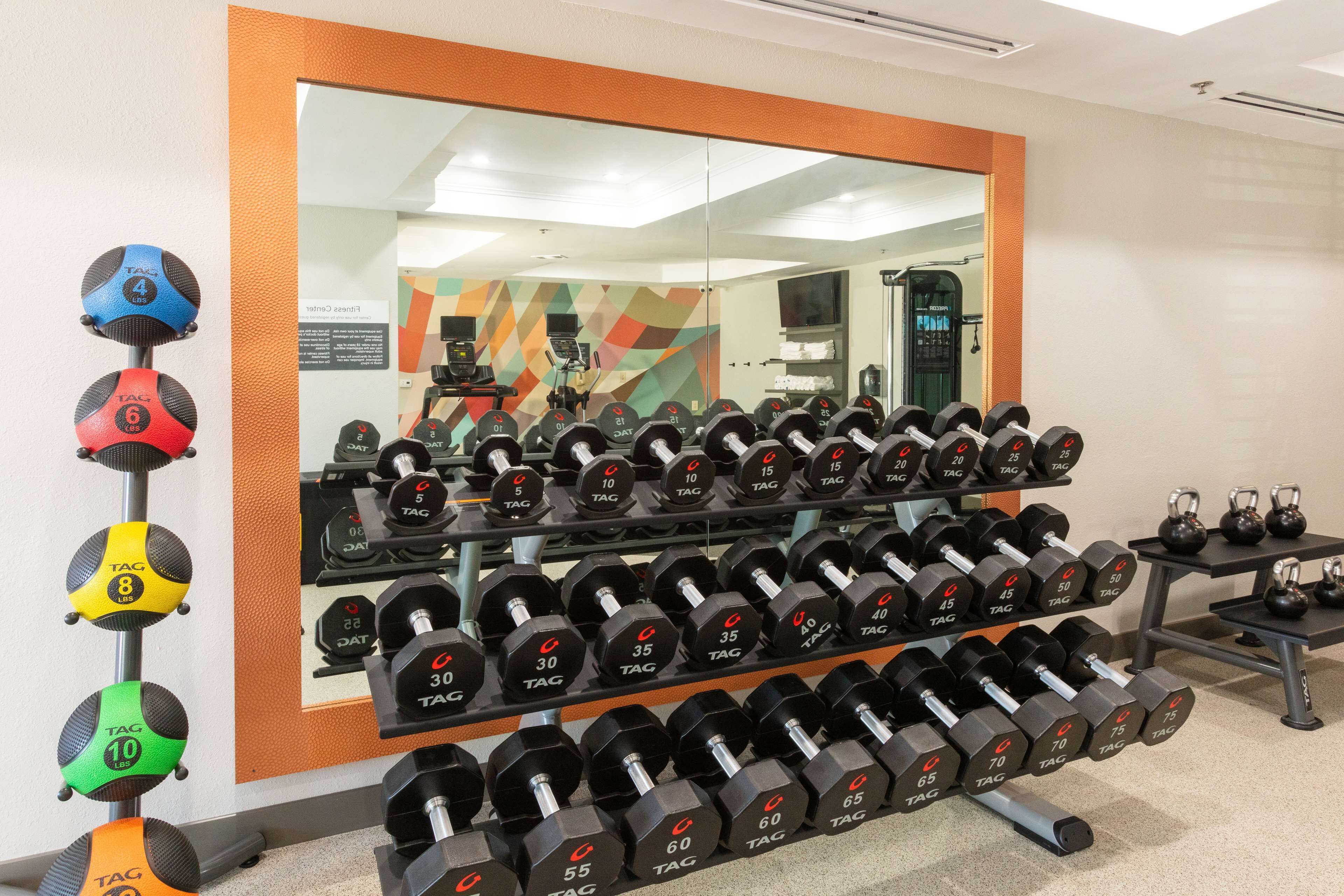 A gym with rows of dumbbells, kettlebells, and a mirror reflecting the room.