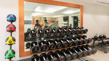A gym with rows of dumbbells, kettlebells, and a mirror reflecting the room.