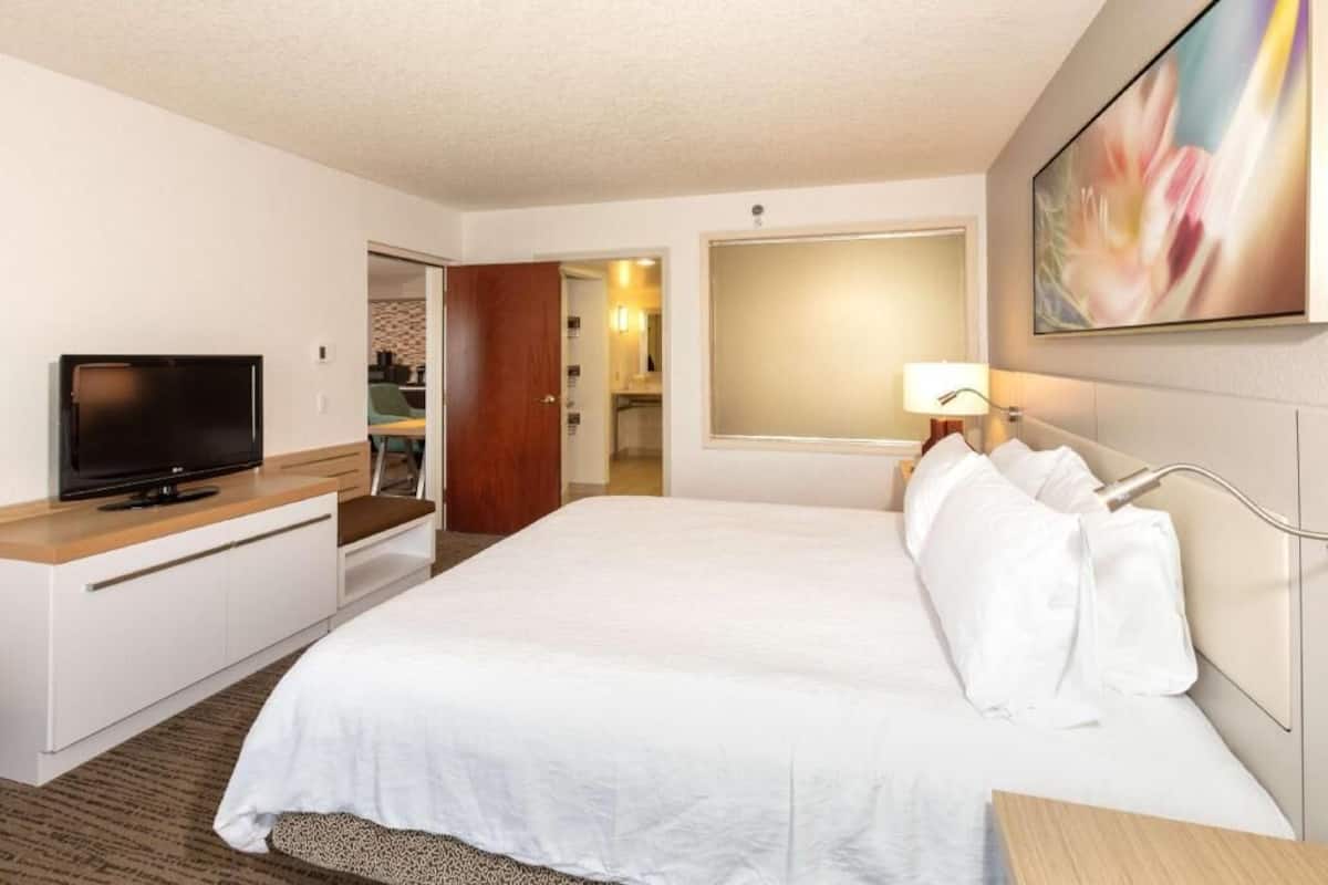 A hotel room with a bed, a television, a desk, and a bathroom visible through an open door.