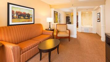 A hotel room with a sofa, armchair, small table, and a painting on the wall.