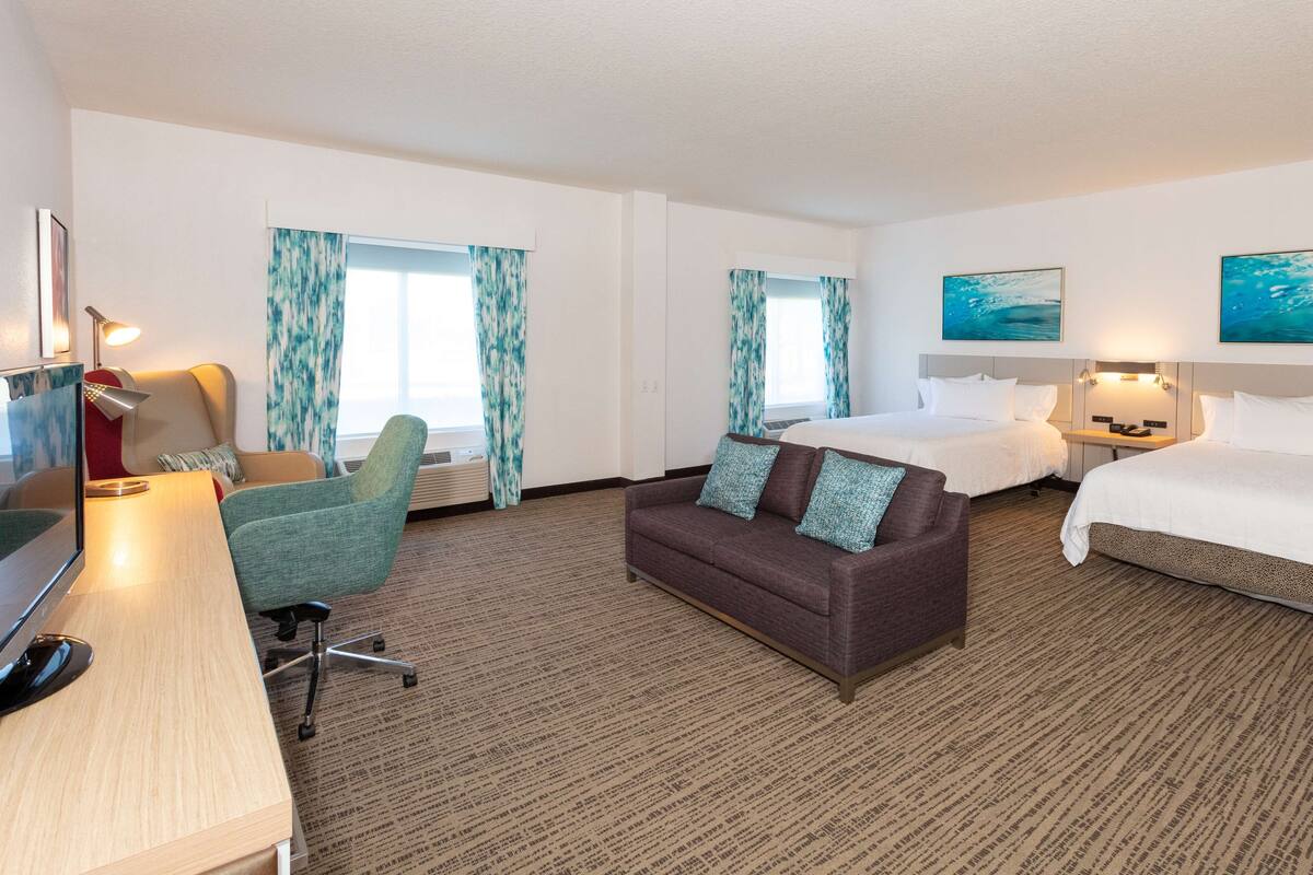 A hotel room with a desk, two couches, a bed, and a TV.