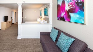 Una habitación de hotel moderna con una cama grande, una zona de estar con sofá y almohadas, un televisor y obras de arte en la pared.