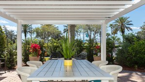 Un espacio de estar techado al aire libre con una mesa y sillas, rodeado de exuberante follaje y palmeras.
