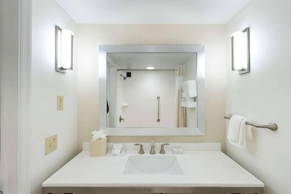 A bathroom with a white sink, a large mirror, and two wall-mounted lights.