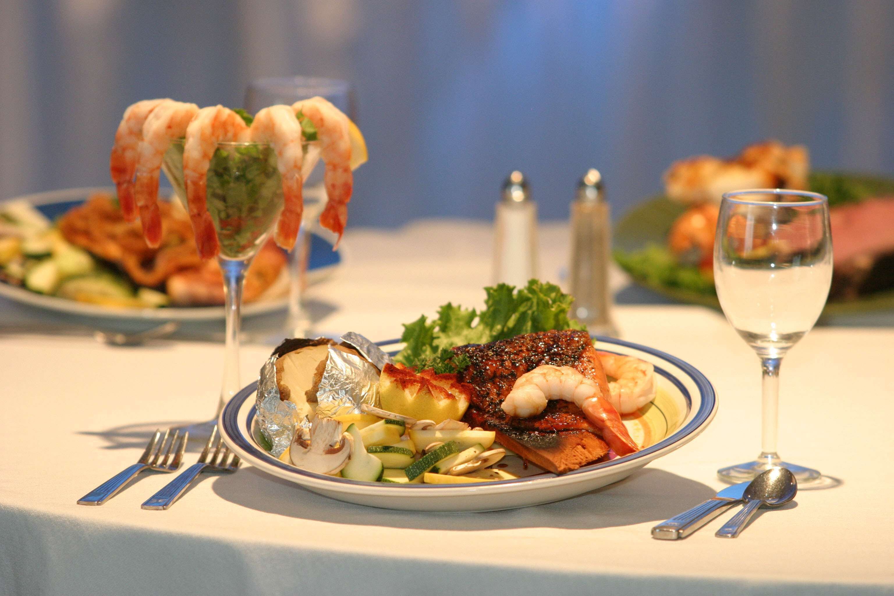 Une table à manger élégamment dressée, avec des assiettes de fruits de mer, un verre de vin blanc et une variété de couverts.