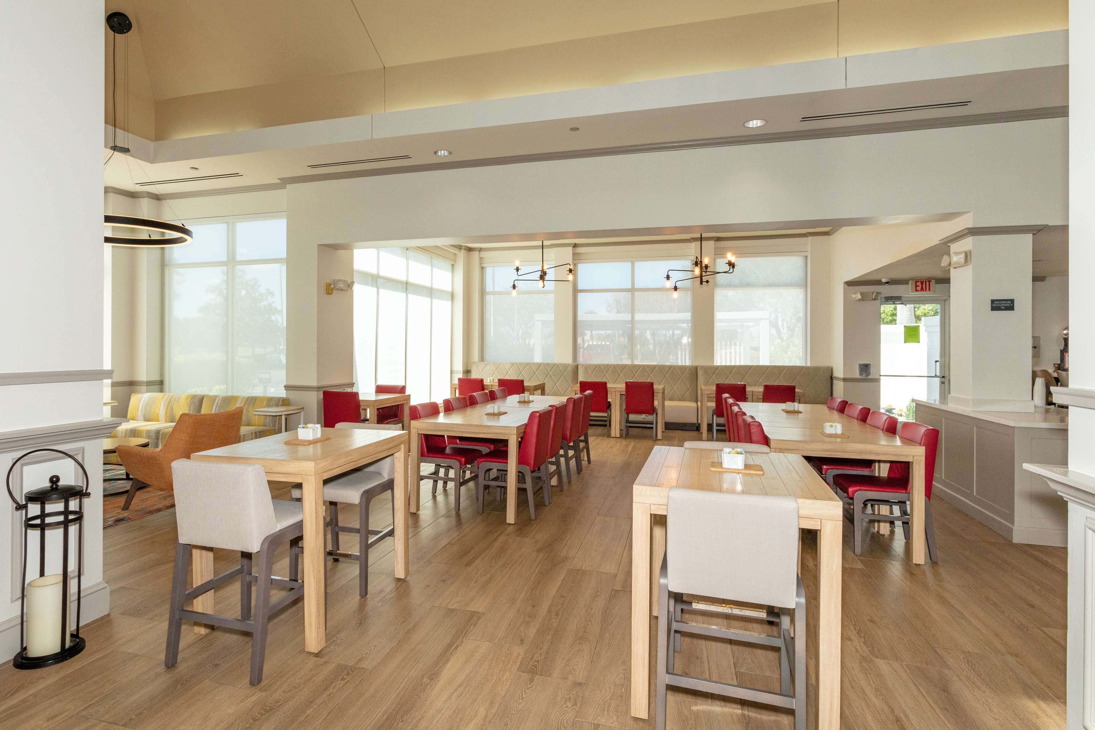 A spacious dining area with multiple tables and chairs, large windows, and a modern chandelier.