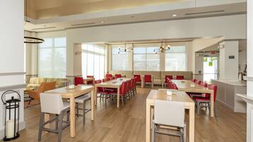 A spacious dining area with multiple tables and chairs, large windows, and a modern chandelier.