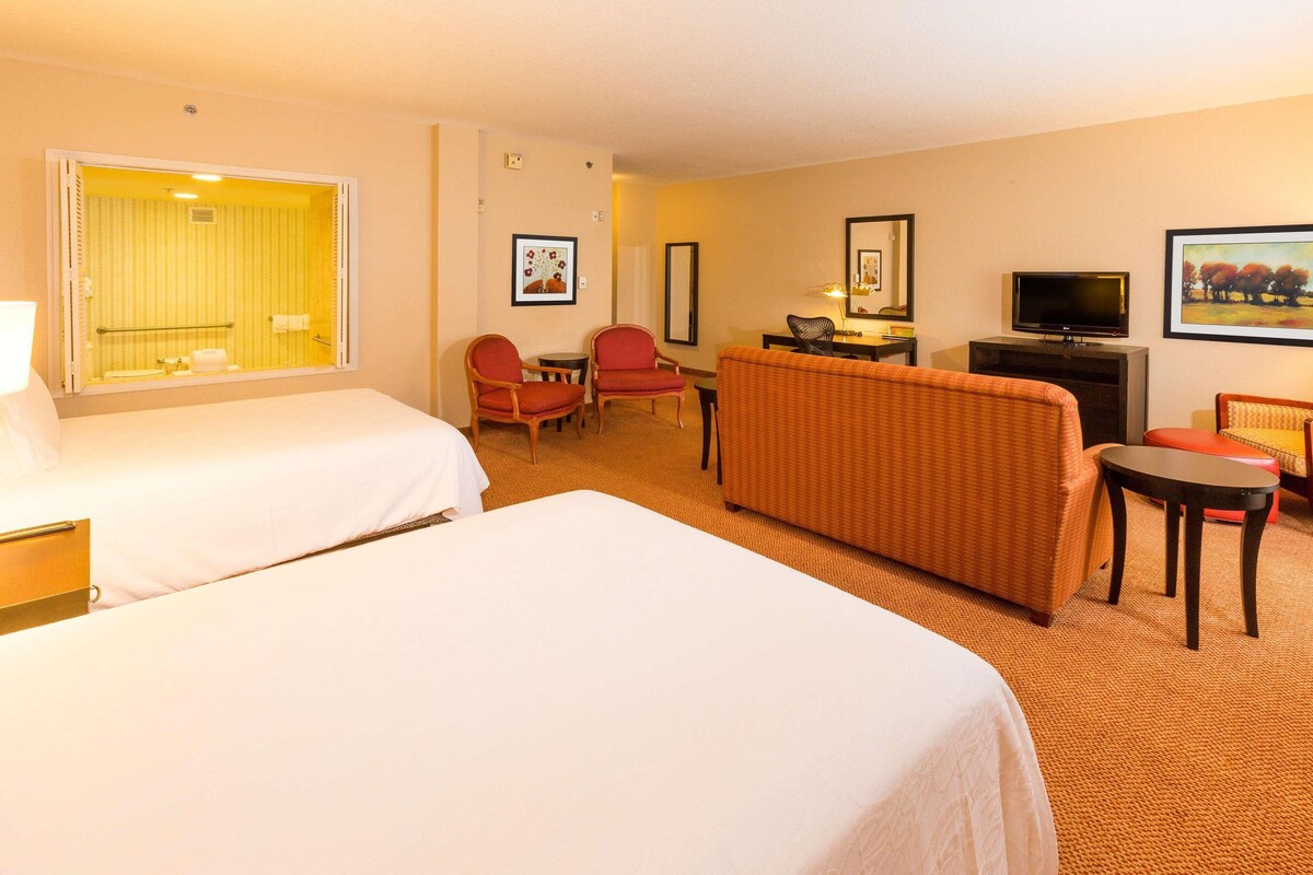 A hotel room with two beds, a sofa, a TV, and a desk with a chair.