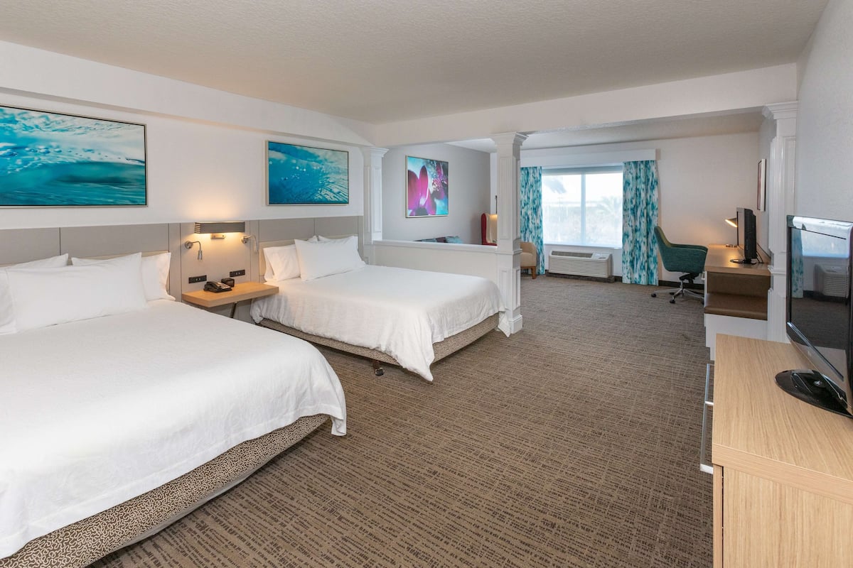 A hotel room with two beds, a desk, a TV, and artwork on the walls.