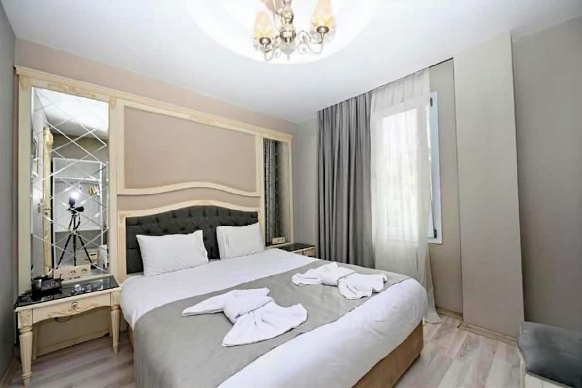 A hotel room with a large bed, a mirror, a desk with a lamp, and a chair.