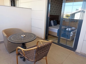 A balcony with a wicker table and chairs, a bed with a blue bedspread, and a view of buildings through a glass door. - Albatros Premier Hotel - Special Class (Istanbul)