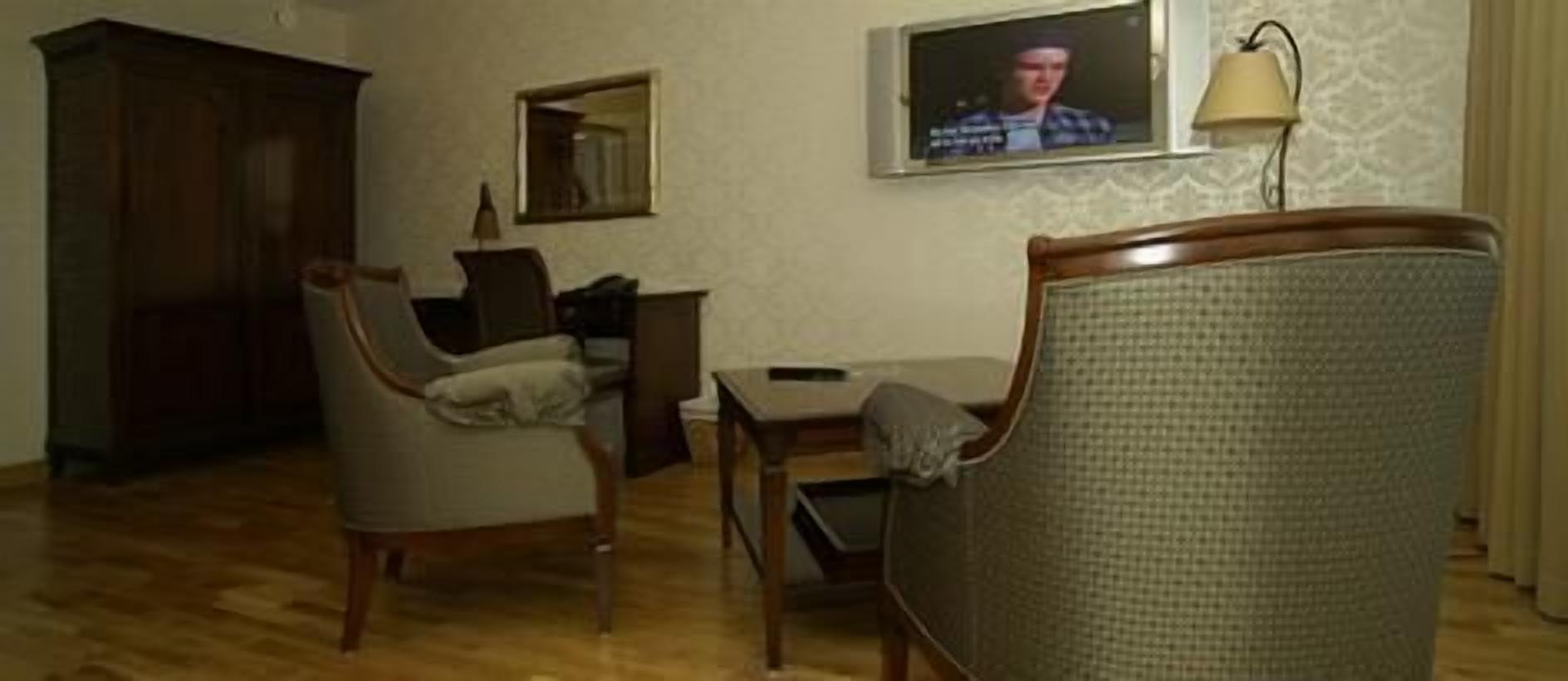 Ett vardagsrum med trägolv, en tv som är monterad på väggen, en lampa och en stol.