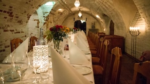 Un comedor abovedado con una larga mesa dispuesta para una comida, con velas y un jarrón de flores.
