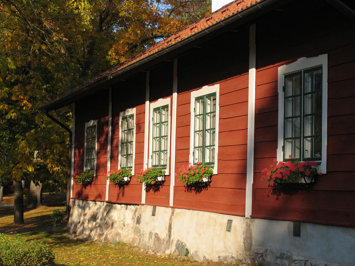 Un edificio de madera roja con detalles blancos y numerosas ventanas, cada una con una maceta de flores.