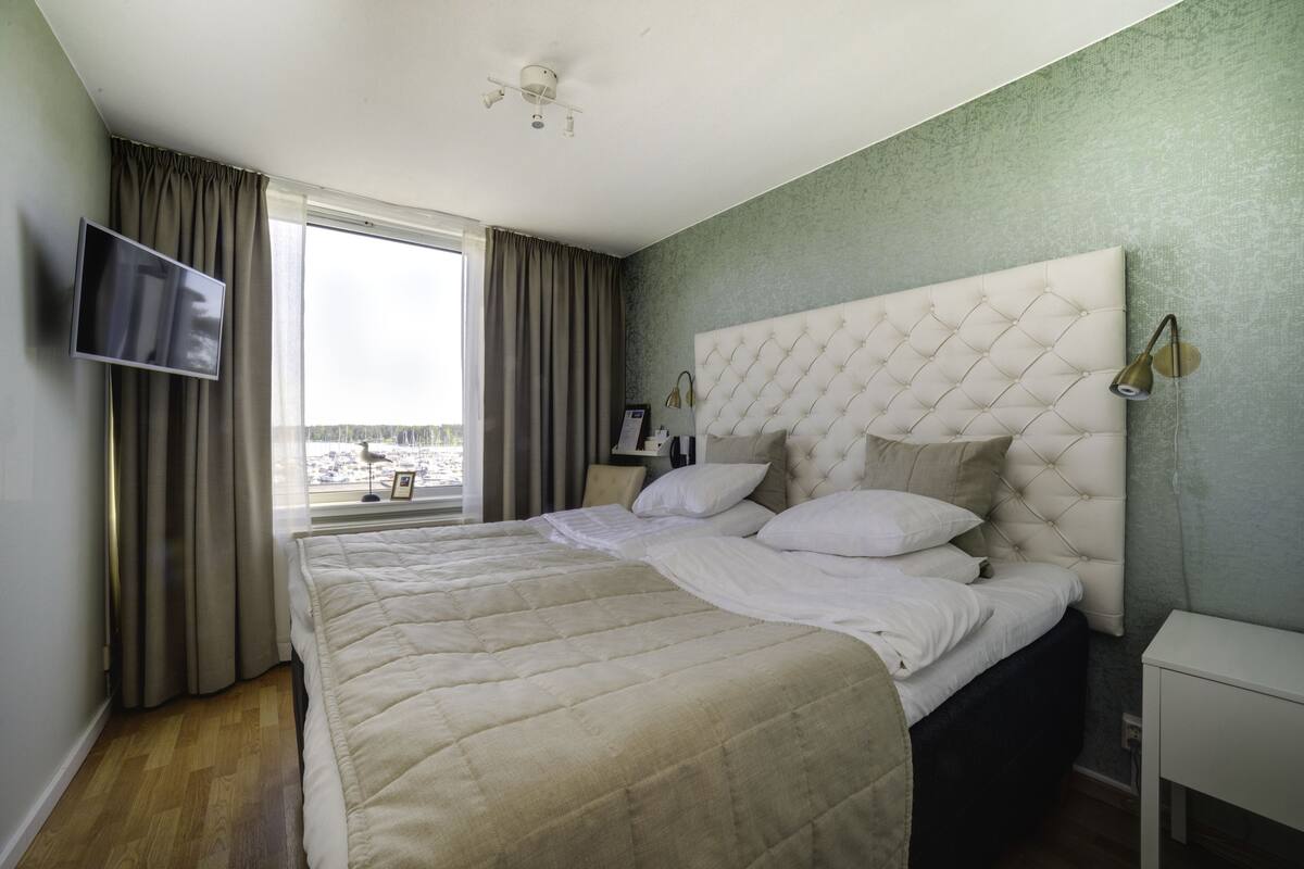 A hotel room with a large bed, a television mounted on the wall, and a window with curtains.