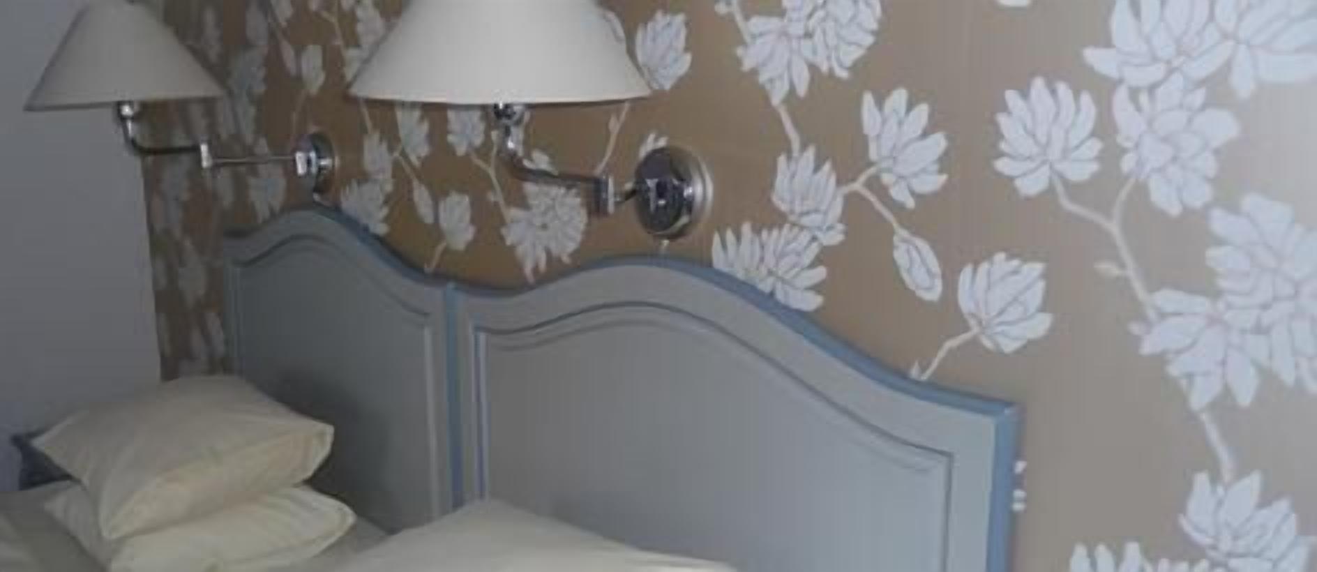 Un dormitorio con una cama, dos lámparas de pared y papel tapiz con motivos florales.