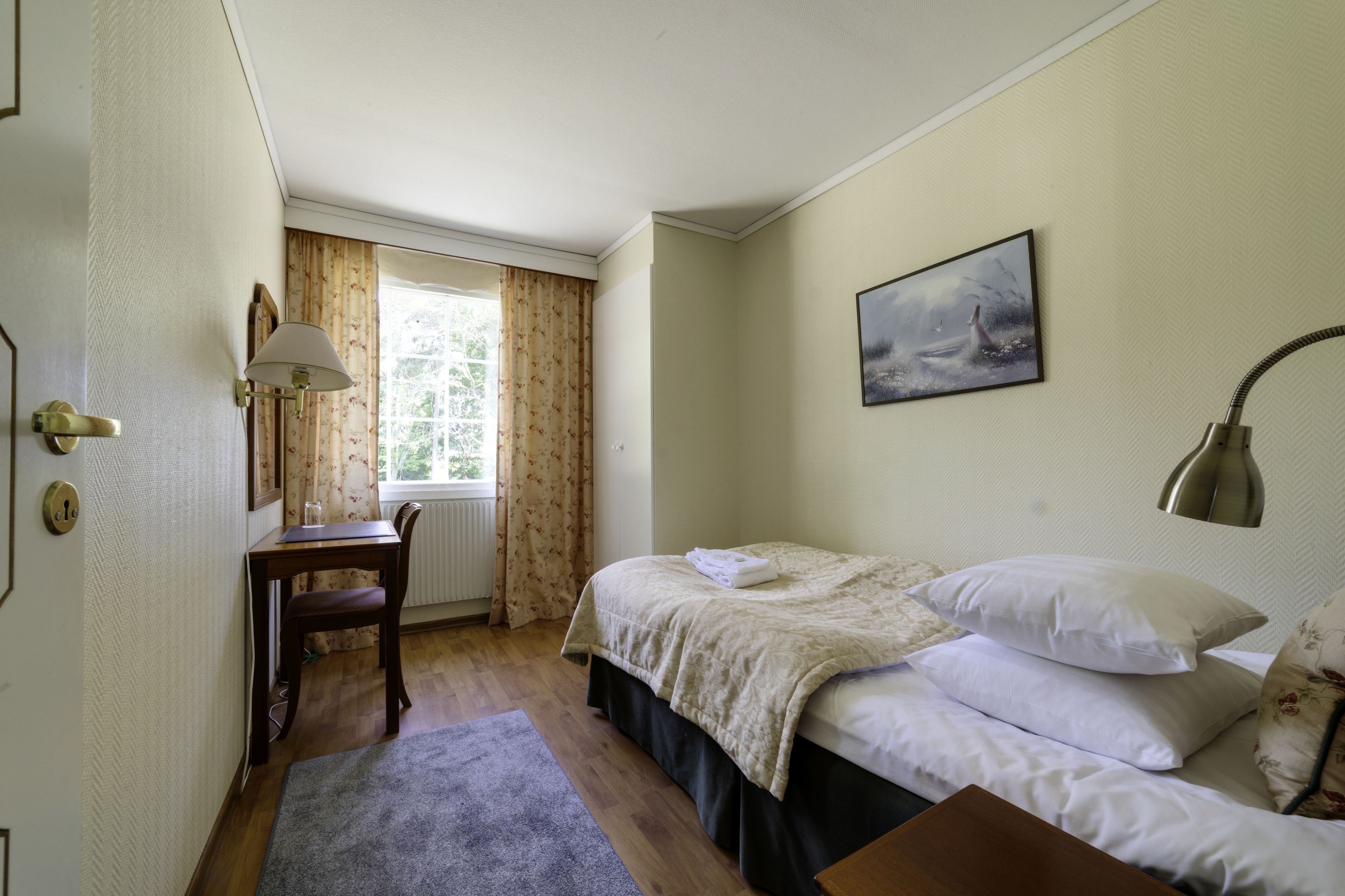 Une chambre à coucher avec un lit, un bureau, une chaise et une fenêtre avec des rideaux.