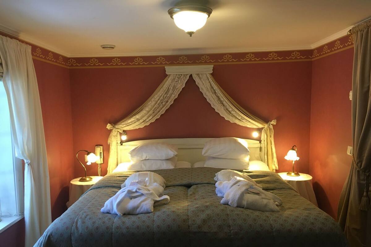 A hotel room with a bed, two bedside lamps, a telephone, and a canopy bed.