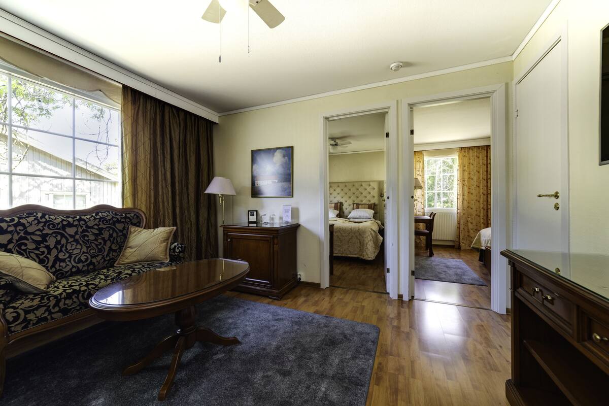 A hotel room with a sofa, a table, a bed, and a bathroom visible through an open door.