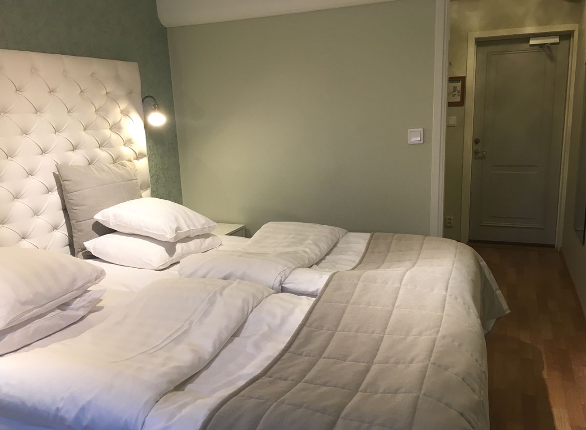 A bedroom with a tufted headboard, two beds with white bedding, a nightstand, and a wall-mounted light.