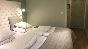 A bedroom with a tufted headboard, two beds with white bedding, a nightstand, and a wall-mounted light.