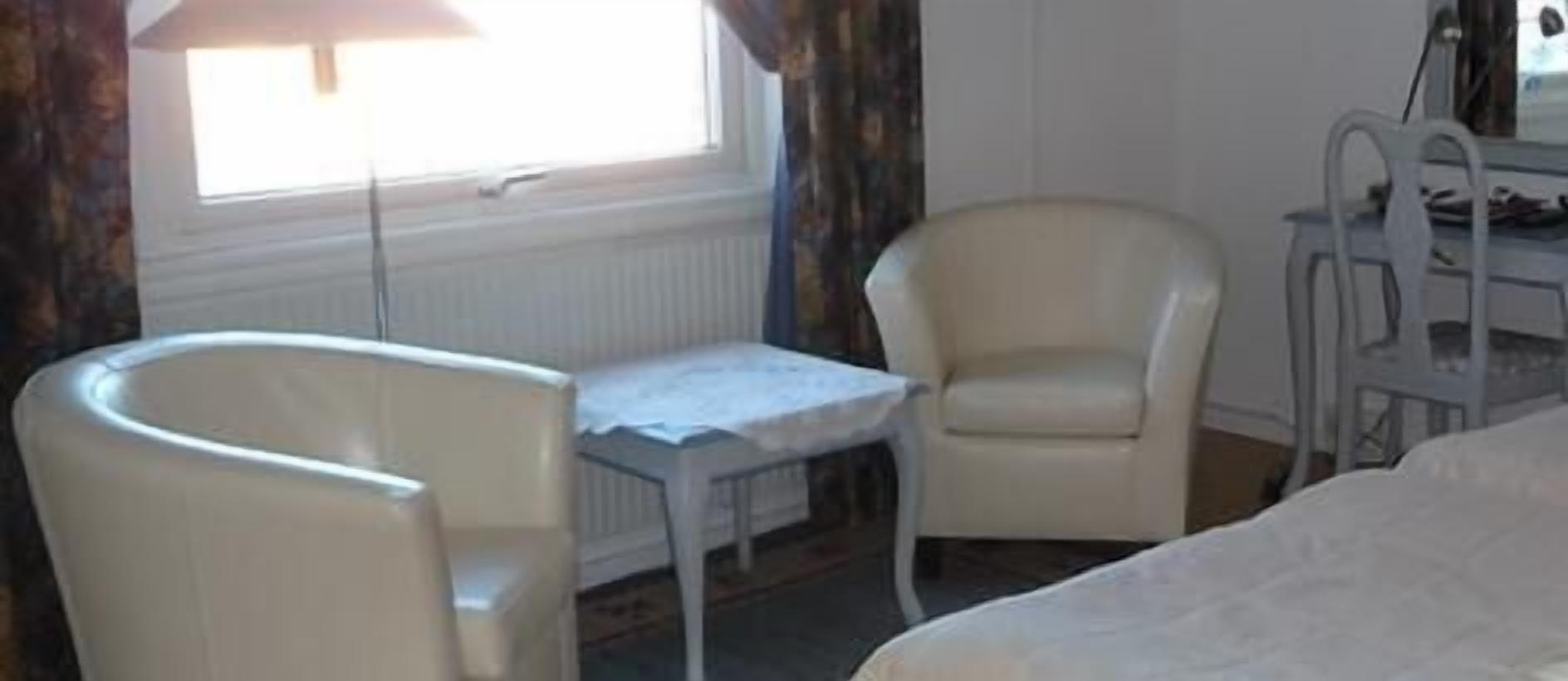 Ett hotellrum med en säng, ett litet bord, två stolar, ett skrivbord och ett fönster med gardiner.