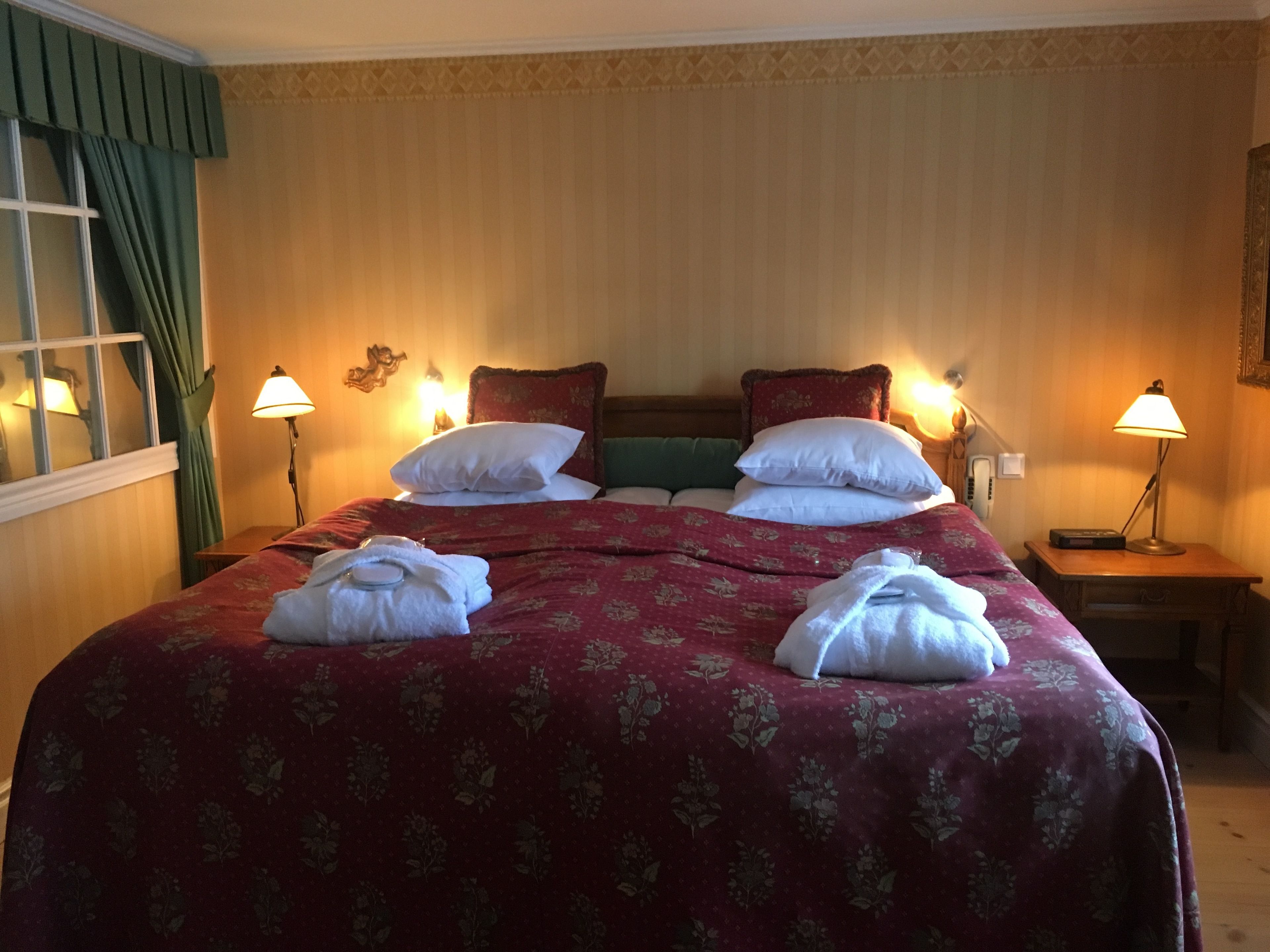 Habitación de hotel con una cama grande, dos lámparas de noche, una mesita de noche y una ventana con cortinas.