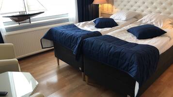 A hotel room with a large bed, two pillows, a bedside lamp, a window with a sailboat model, a chair, and a small table.