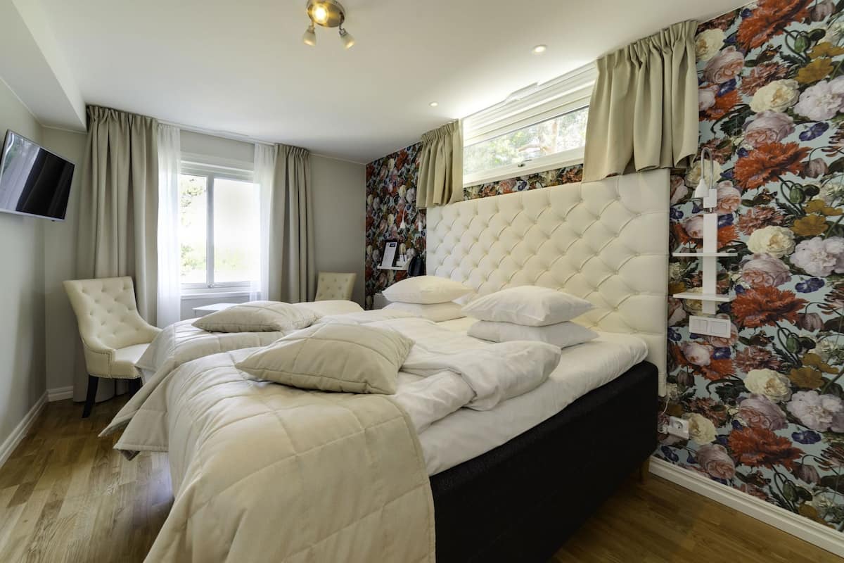 A bedroom with a large bed, a chair, a television, and a floral wallpaper.