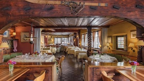 A restaurant with wooden tables and chairs, a checkered floor, and a high ceiling with exposed beams. - Hotel Chesa Grischuna (Klosters-Serneus)