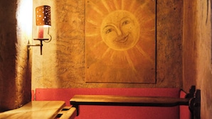 A dimly lit room with a mural of a smiling sun on the wall, a red cushioned bench, and a small table with a lamp. - Hotel Chesa Grischuna (Klosters-Serneus)
