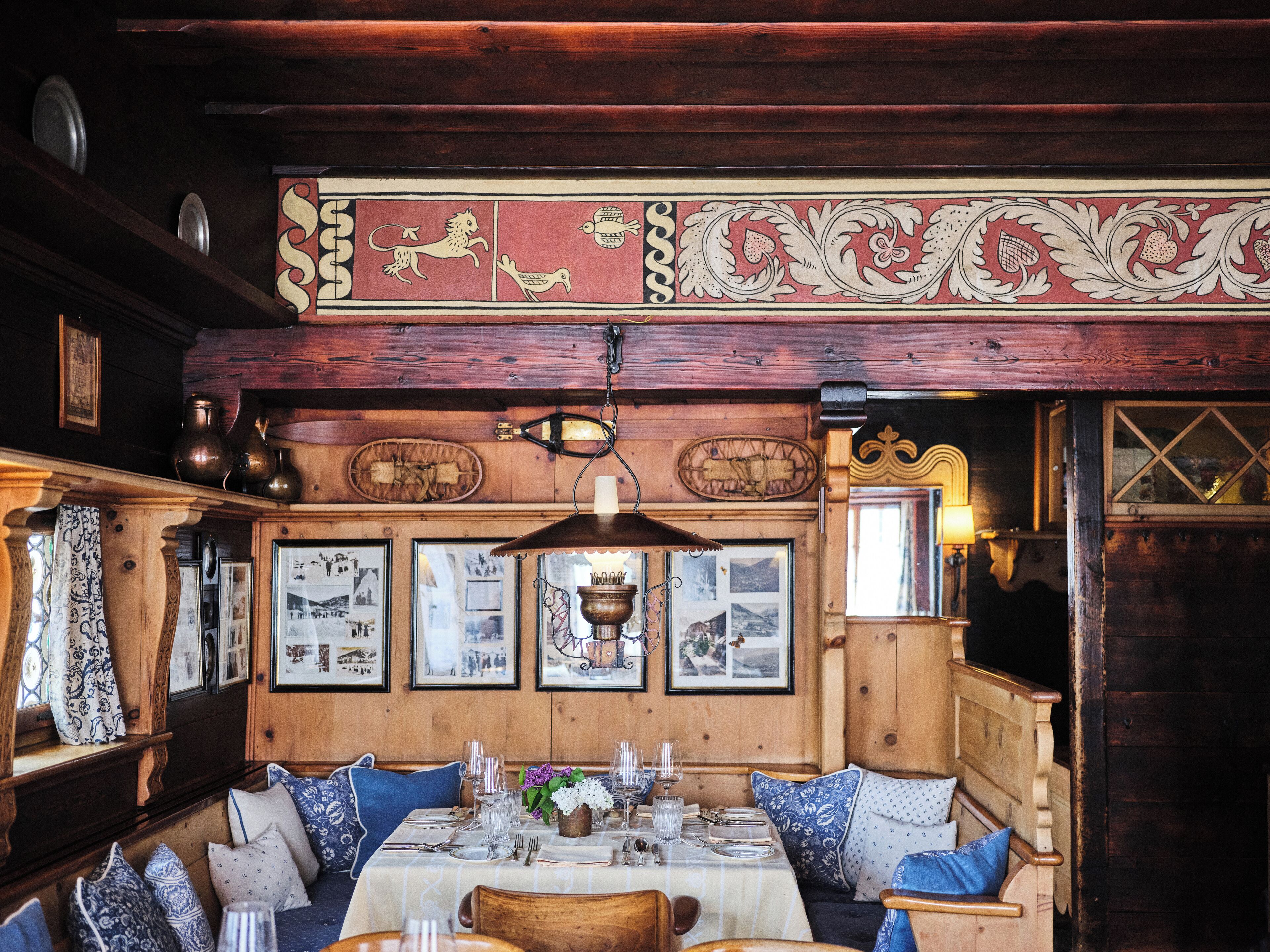 A rustic wooden interior with a long communal table, benches, and framed pictures on the walls.