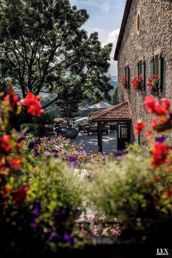 Een stenen gebouw met een overdekt terras en uitzicht op bomen en bergen.