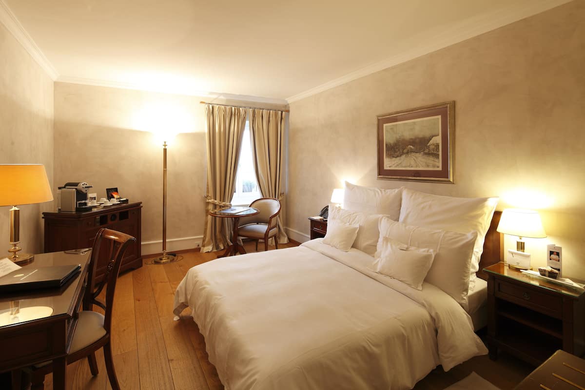Une chambre d’hôtel avec un lit, un bureau, une chaise, une lampe, une table de chevet et un tableau au mur.