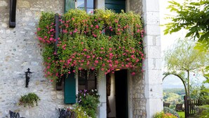 Un edificio de piedra con un porche cubierto, contraventanas verdes y vistas al campo.
