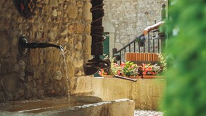 Un edificio rústico de piedra con una escalera de madera que lleva a un ventanal con contraventanas verdes.