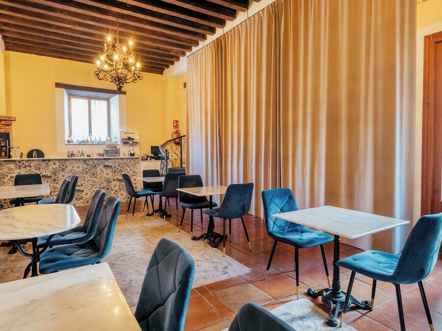 A restaurant with marble-topped tables and blue upholstered chairs, a chandelier, and a window with curtains.