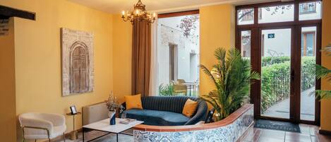 Una sala de estar con sofá, una mesa de centro, una silla, una araña y un ventanal con vistas al exterior.
