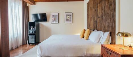 Un dormitorio con una cama grande, televisor, cuadros enmarcados y cabecera de madera.