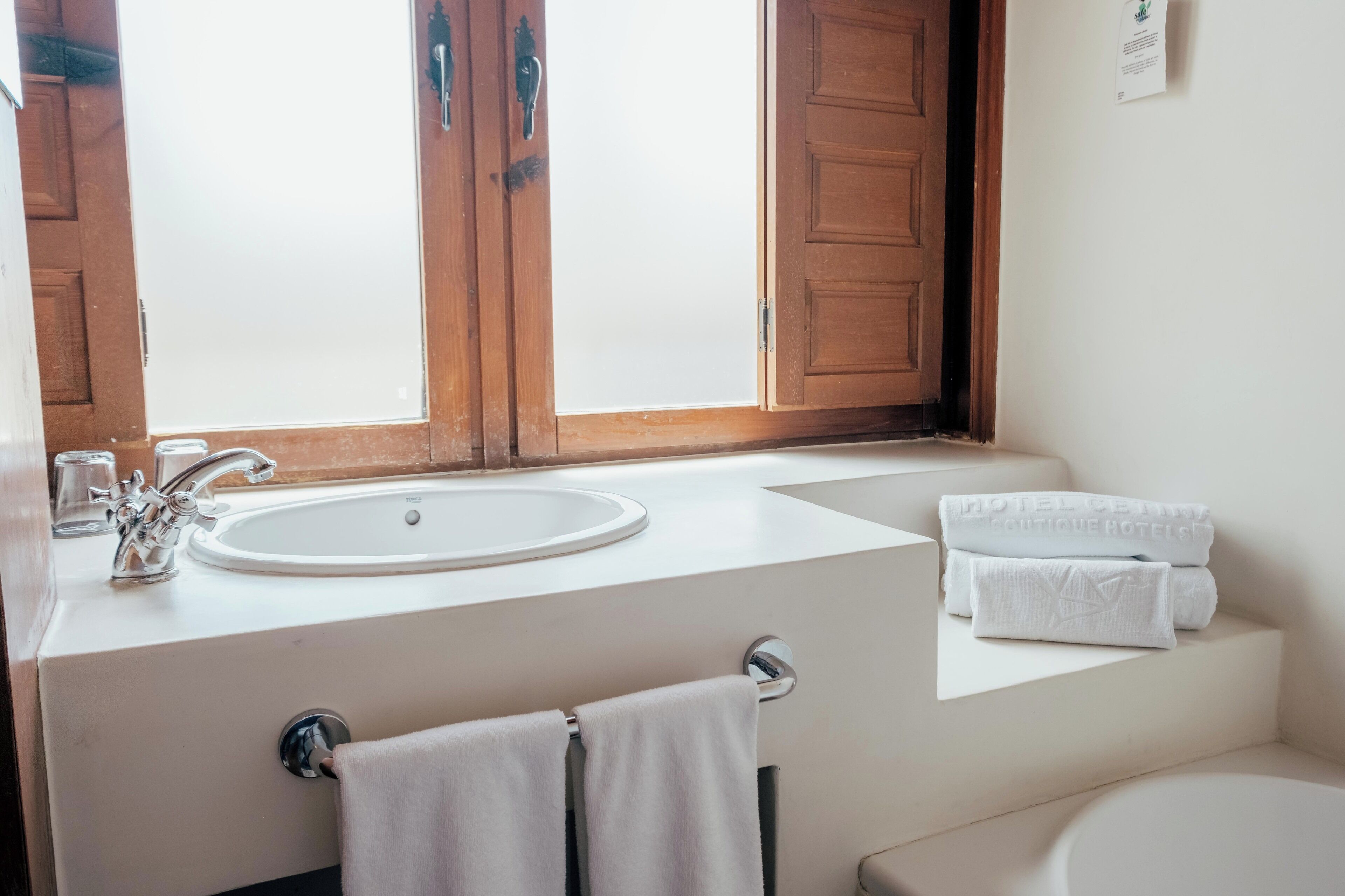 A bathroom with a sink, towel rack, and a window with wooden shutters.