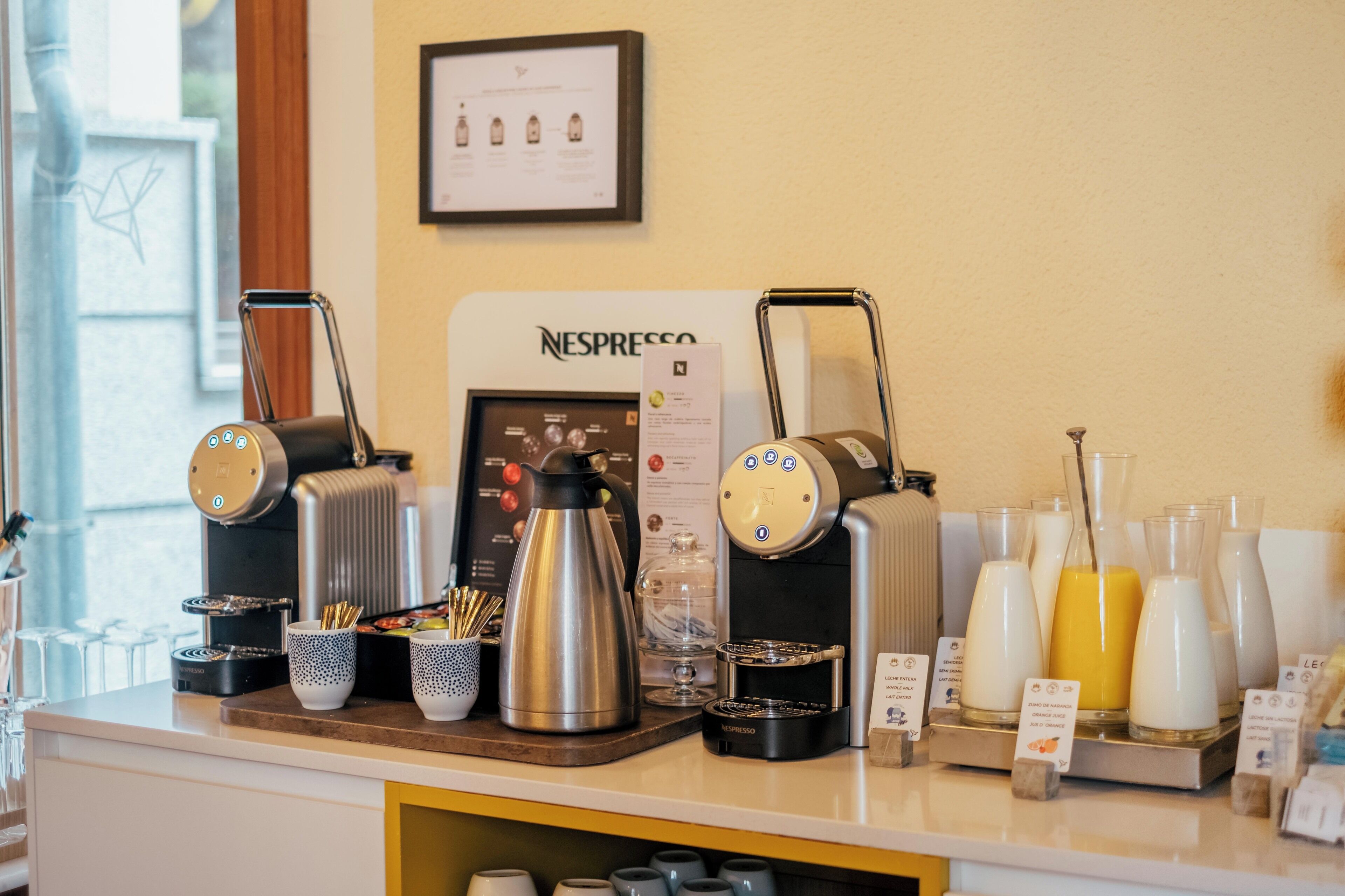A coffee station with a Nespresso machine, coffee pots, milk dispensers, and a variety of coffee cups and mugs.